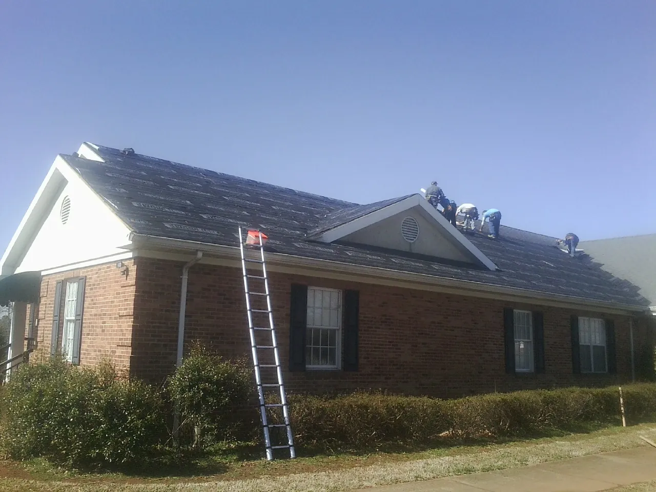 Crew tearing shingles off a brick ranch roof with a ladder set — Metal Roof Repair work by our crew in New Market