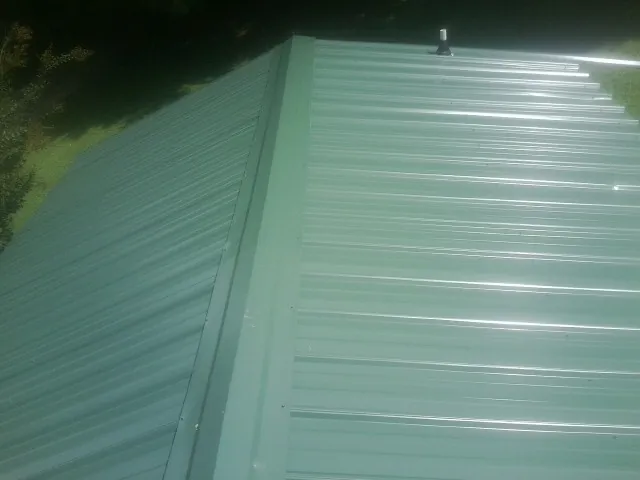 New green metal panels meeting at the ridge of a roof — Flat Roof Repair work by our crew in New Market