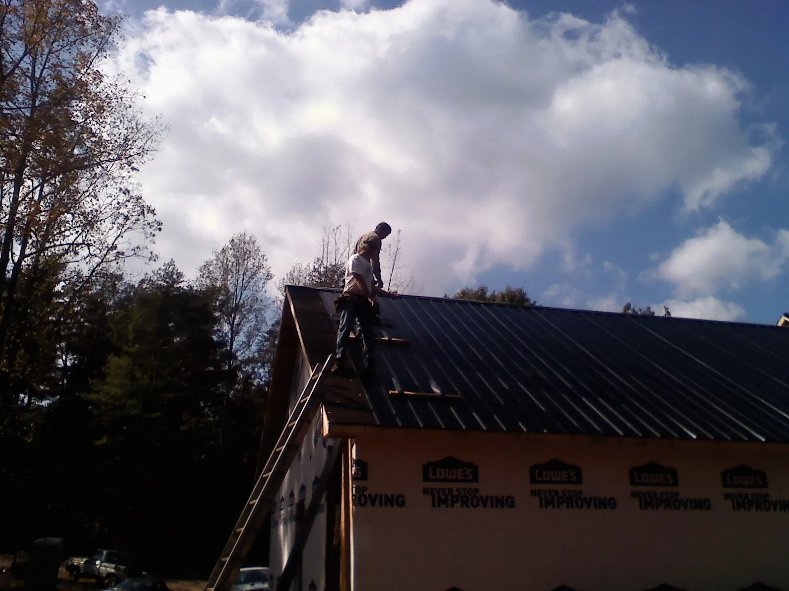 Roofer fastening dark metal panels high against a cloudy sky, from a Roof Inspection job in New Market